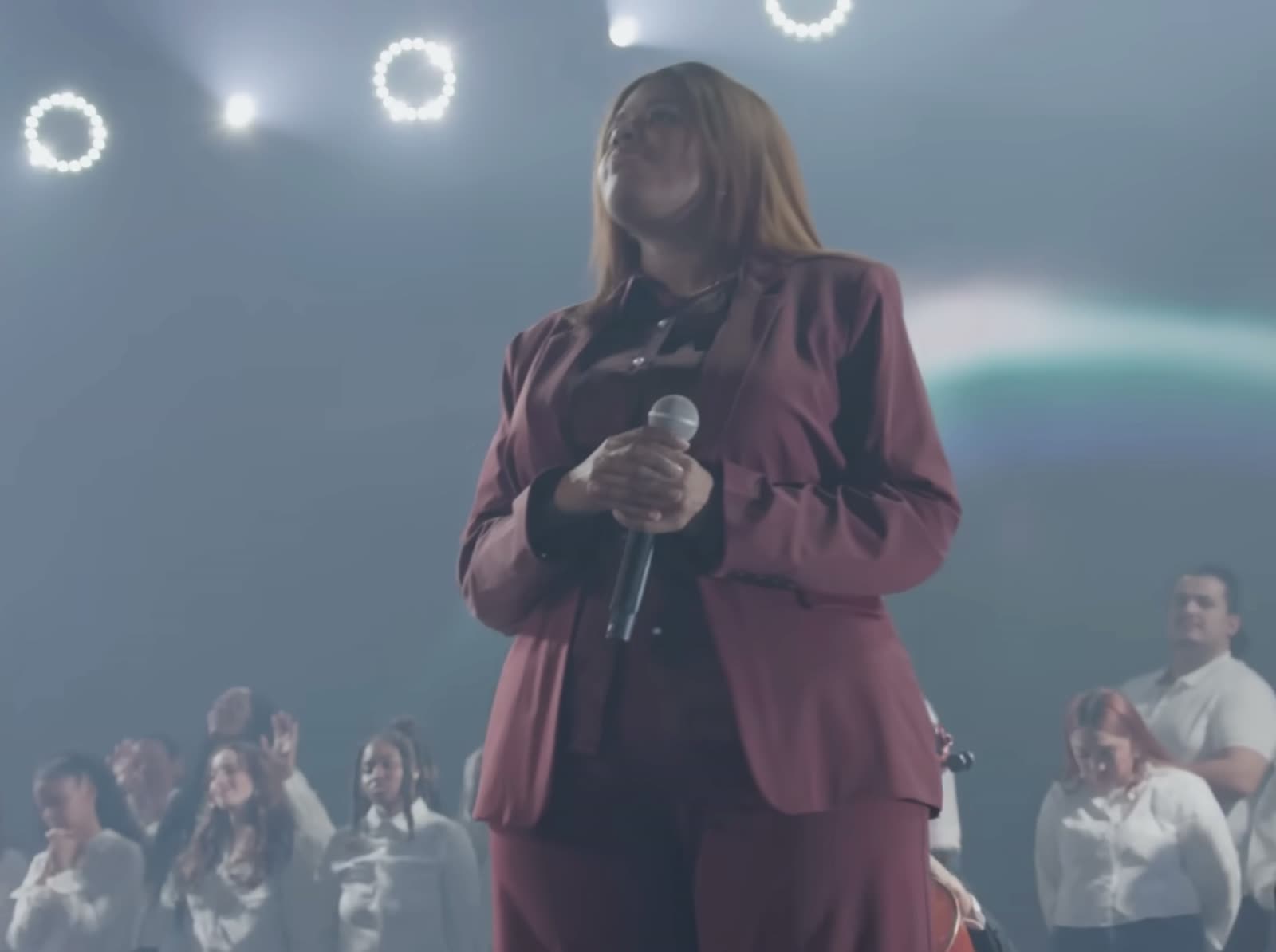 Naomi Raine singing on stage with choir behind her